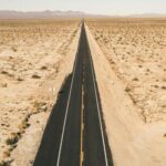 A vast landscape featuring a long, straight highway stretching into the horizon across the American desert.