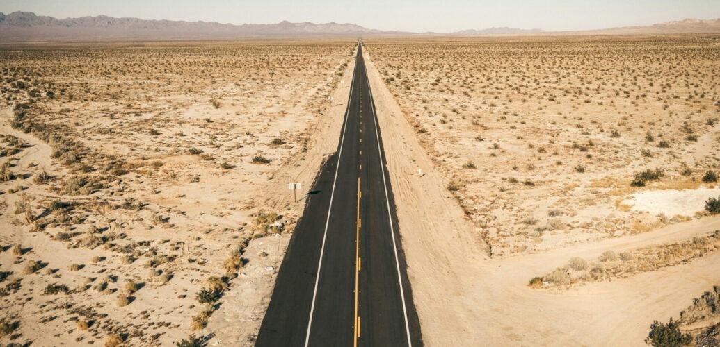 A vast landscape featuring a long, straight highway stretching into the horizon across the American desert.