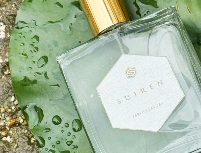 A close-up shot of the SUIREN perfume bottle set gracefully upon a smooth, wet water lily leaf floating on water.